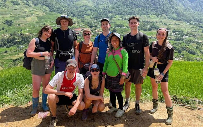 Group of trekkers with local guide on Sapa's Y Linh Ho trail, rice terraces in background.
