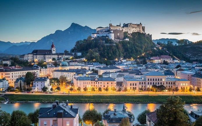 Salzburg cityscape with Hohensalzburg Fortress at dusk, view from the river.