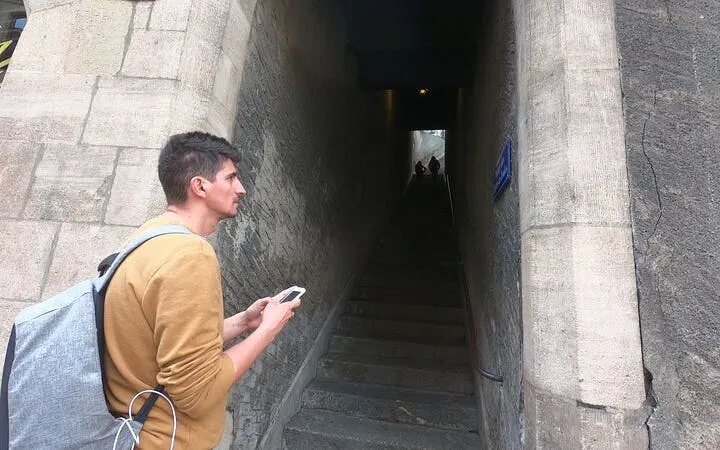 Man with smartphone exploring narrow stone passage in Geneva city game.