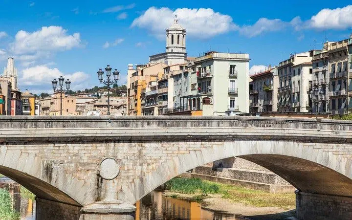 Girona cityscape with Onyar River bridge and colorful buildings, viewed on a self-guided walking tour.