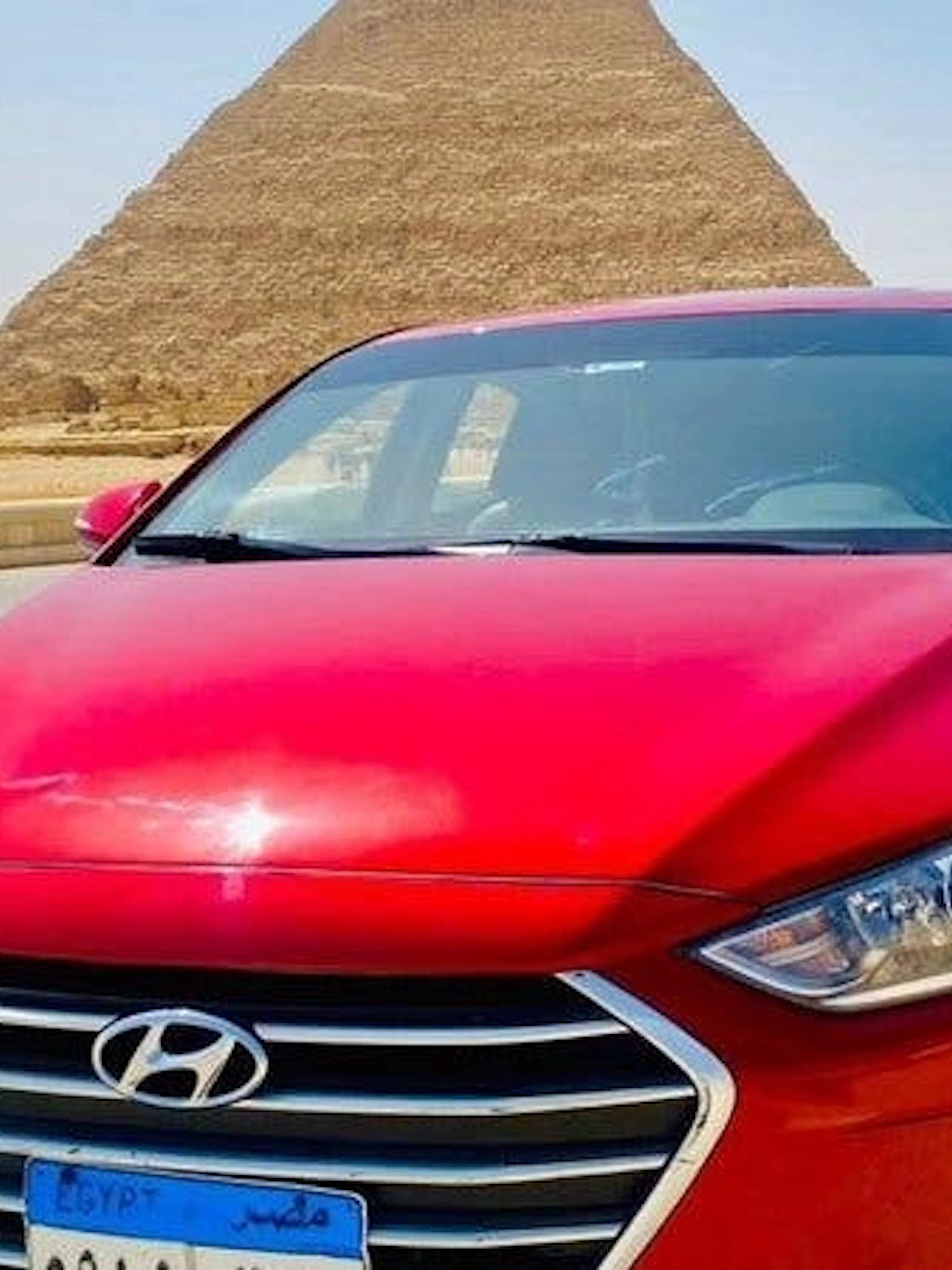 Red car in front of the Pyramids of Giza, Cairo, for private airport or hotel transfer.