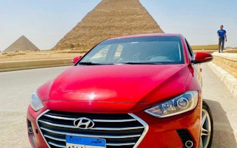 Red car in front of the Pyramids of Giza, Cairo, for private airport or hotel transfer.