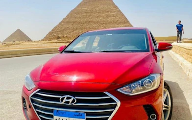 Red car in front of the Pyramids of Giza, Cairo, for private airport or hotel transfer.