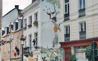 Brussels street with comic mural depicting characters climbing a tree, part of self-guided city exploration game.