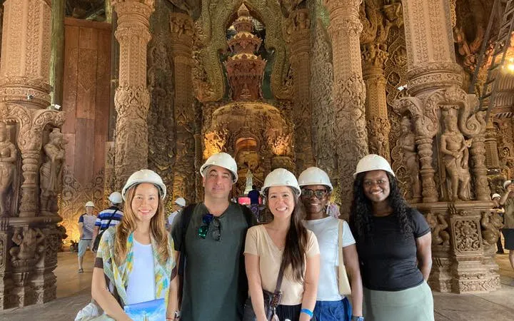 Visitors wearing helmets inside the Sanctuary of Truth, Pattaya, with intricate wooden carvings.
