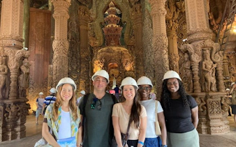 Visitors wearing helmets inside the Sanctuary of Truth, Pattaya, with intricate wooden carvings.