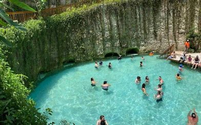 Visitors swimming in a blue lagoon cenote surrounded by lush greenery in Punta Cana.