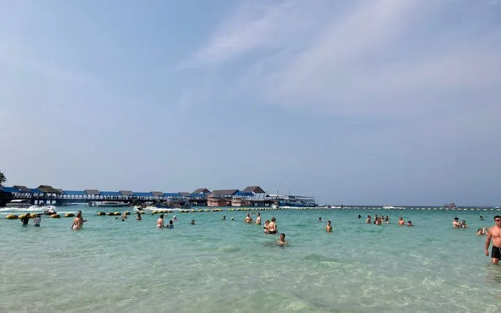 Tourists swimming at Coral Island beach, Pattaya, with distant view of beachfront buildings.