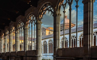 Leaning Tower of Pisa and Cathedral view through arches at sunset, Pisa, Italy.
