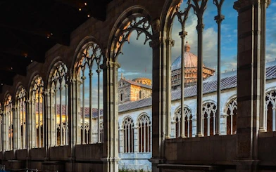 Leaning Tower of Pisa and Cathedral view through arches at sunset, Pisa, Italy.