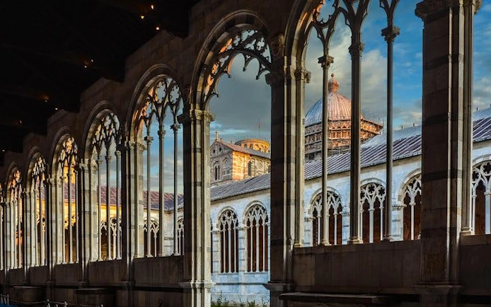 Leaning Tower of Pisa and Cathedral view through arches at sunset, Pisa, Italy.