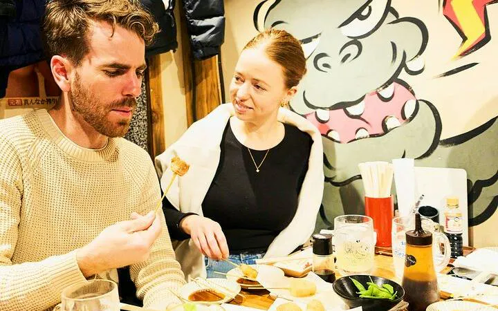 Couple enjoying skewers at a local eatery in Shinjuku during a guided food tour, Tokyo.