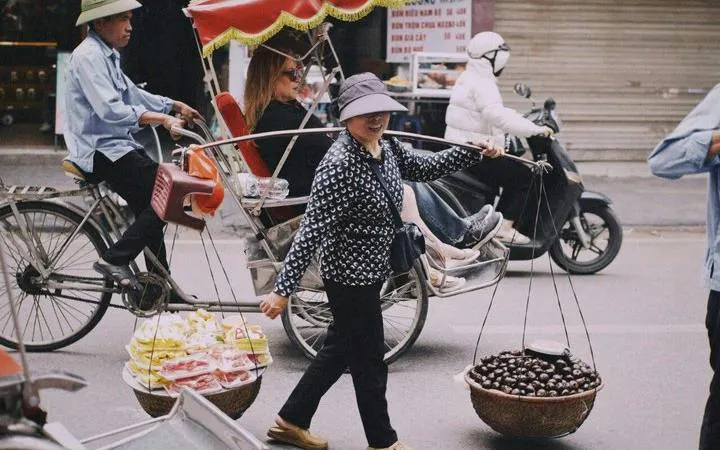 Cyclo ride through Hanoi's Old Quarter with street vendor carrying fruit baskets.