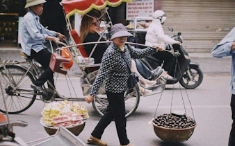 Cyclo ride through Hanoi's Old Quarter with street vendor carrying fruit baskets.