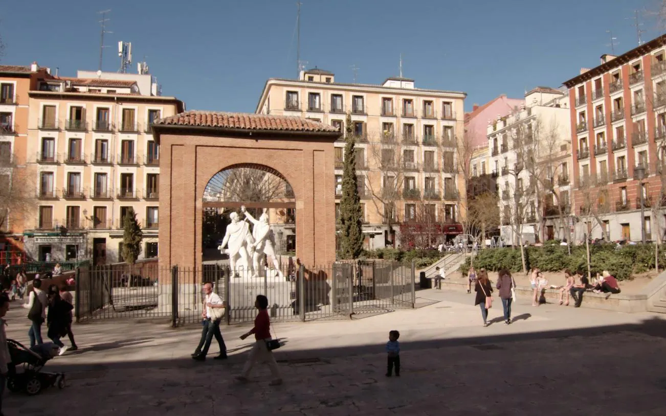 Plaza del Dos de Mayo in Madrid's Malasaña district with people walking and a statue in the center.