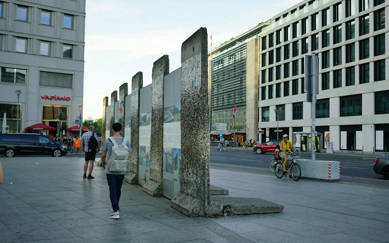 Berlin Wall remnants near Checkpoint Charlie, with pedestrians and cyclists in the cityscape.