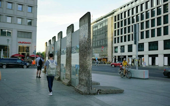 Berlin Wall remnants near Checkpoint Charlie, with pedestrians and cyclists in the cityscape.