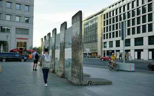 Berlin Wall remnants near Checkpoint Charlie, with pedestrians and cyclists in the cityscape.