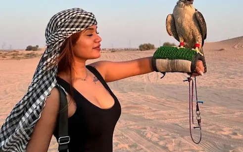 Falcon perched on a woman's gloved hand in Abu Dhabi desert during safari experience.