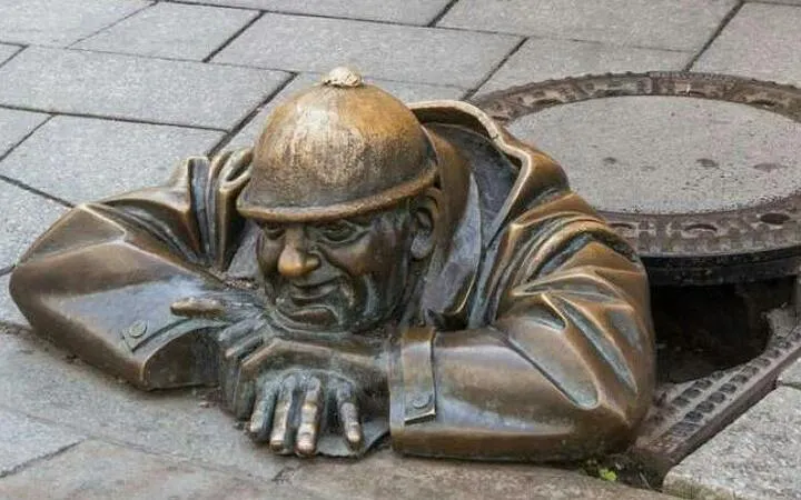 Bronze statue of a man peeking from a manhole in Bratislava, Slovakia.