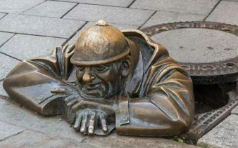 Bronze statue of a man peeking from a manhole in Bratislava, Slovakia.