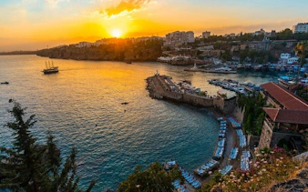 Antalya harbor at sunset with boats and cityscape, part of self-guided walking tour.