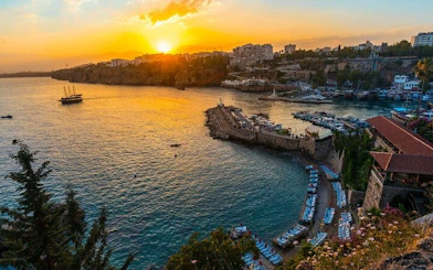Antalya harbor at sunset with boats and cityscape, part of self-guided walking tour.