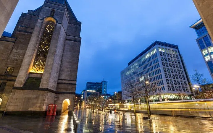 Manchester cityscape at dusk with illuminated buildings and wet streets.