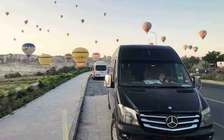 Van parked on roadside with hot air balloons in Cappadocia sky, Turkey.