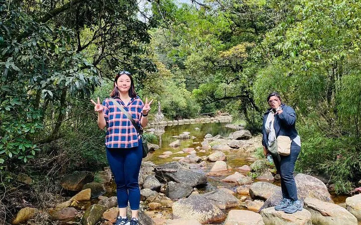 Two people standing on rocks by a stream in a lush Sapa valley during a guided motorbike tour.