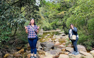 Two people standing on rocks by a stream in a lush Sapa valley during a guided motorbike tour.
