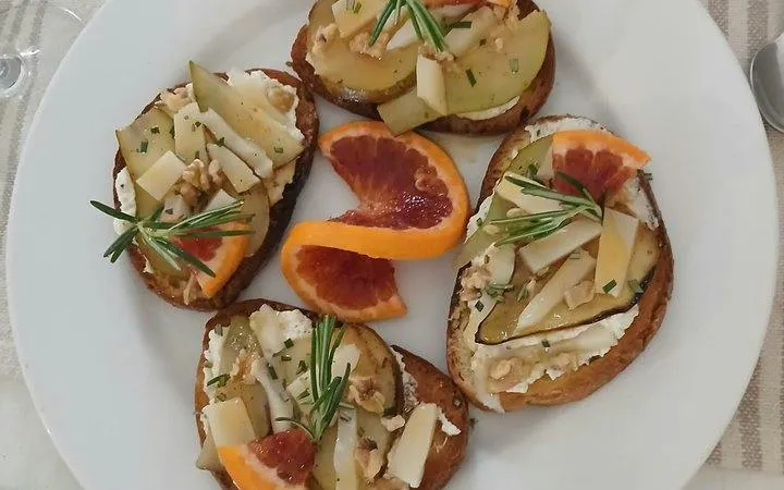 Crostini with cheese, pear, and blood orange slices on a plate, part of Sicilian cooking class in Catania.