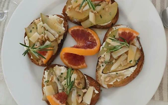 Crostini with cheese, pear, and blood orange slices on a plate, part of Sicilian cooking class in Catania.