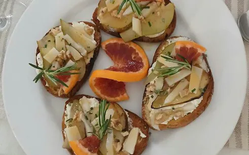 Crostini with cheese, pear, and blood orange slices on a plate, part of Sicilian cooking class in Catania.