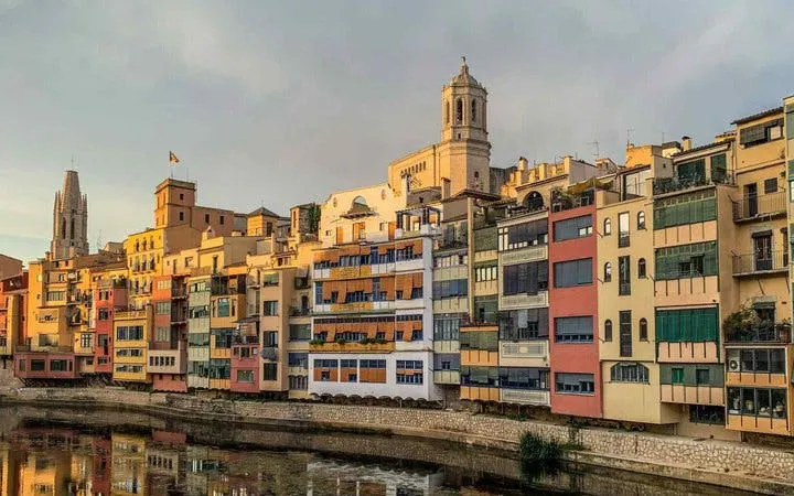 Colorful buildings along the Onyar River in Girona, Spain, with a cathedral in the background.