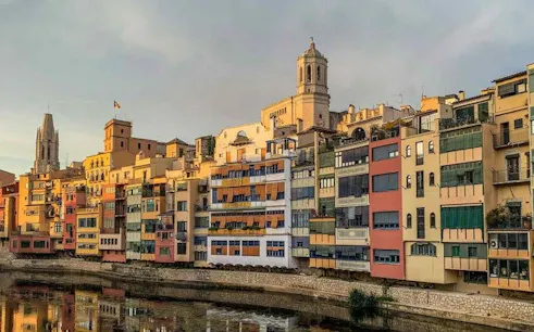 Colorful buildings along the Onyar River in Girona, Spain, with a cathedral in the background.