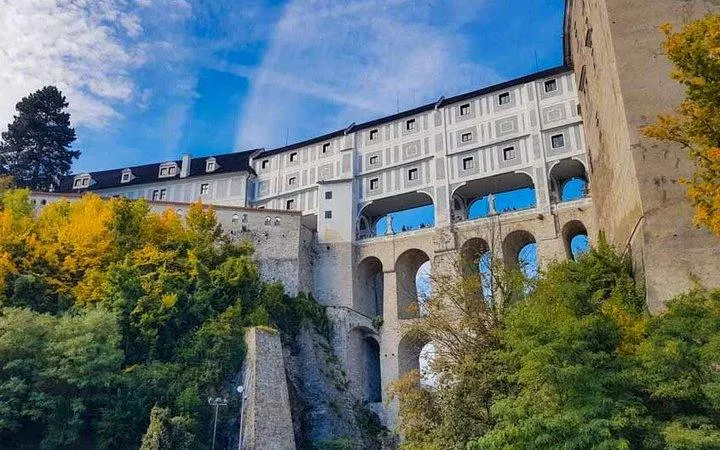 Český Krumlov Castle with arched bridge and autumn trees, stop on Salzburg to Prague transfer.