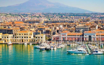 Catania harbor with boats and Mount Etna in the background, part of a self-guided walking tour.