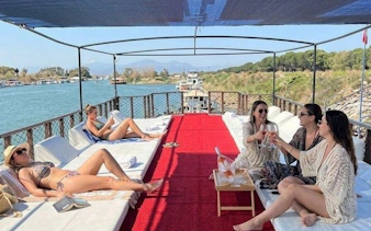 Boat tour in Antalya with people relaxing and enjoying drinks, surrounded by scenic river views.