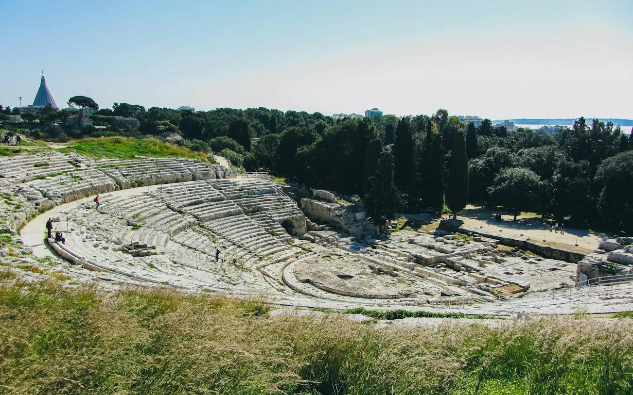 Ancient Greek Theatre in Neapolis Archaeological Park, Syracuse, surrounded by greenery.