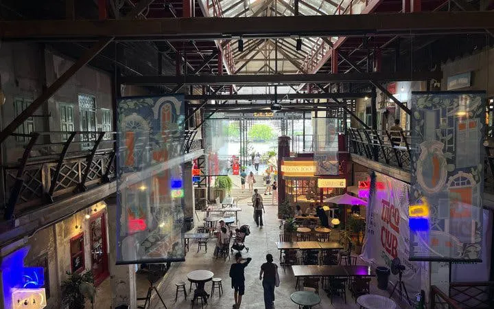 Indoor view of Talat Noi market in Bangkok with people walking, colorful signs, and dining tables.