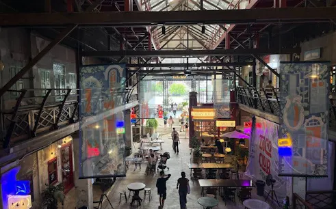 Indoor view of Talat Noi market in Bangkok with people walking, colorful signs, and dining tables.