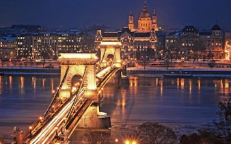 Chain Bridge illuminated at night in Budapest, with St. Stephen's Basilica in the background.