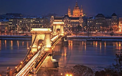 Chain Bridge illuminated at night in Budapest, with St. Stephen's Basilica in the background.