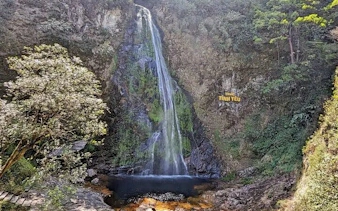 Waterfall cascading down rocky cliff surrounded by lush greenery in Sapa, Vietnam.