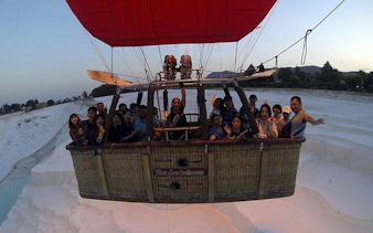 Hot air balloon with passengers over Pamukkale travertines at sunrise, Turkey.