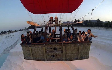 Hot air balloon with passengers over Pamukkale travertines at sunrise, Turkey.