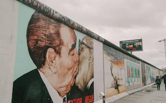 Berlin Wall murals at East Side Gallery featuring "The Kiss" near Oberbaum Bridge.