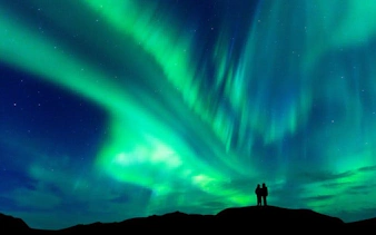 Northern Lights over Iceland with silhouetted figures on a hill during a self-guided walking tour.