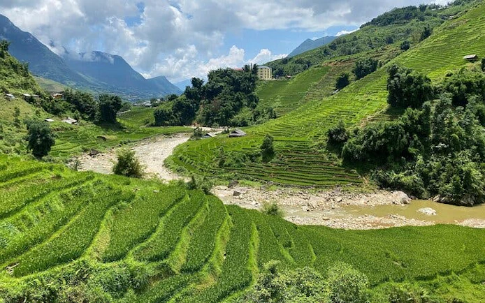 Terraced rice fields in Sapa, Vietnam, with mountains and a river in the background.